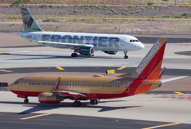 Airbus A320 (N207FR) - Frontier A320 taking the runway to depart while Southwest's "Herbert D. Kelleher" N711HK retro taxis out for departure (View in "full" for highest image quality)