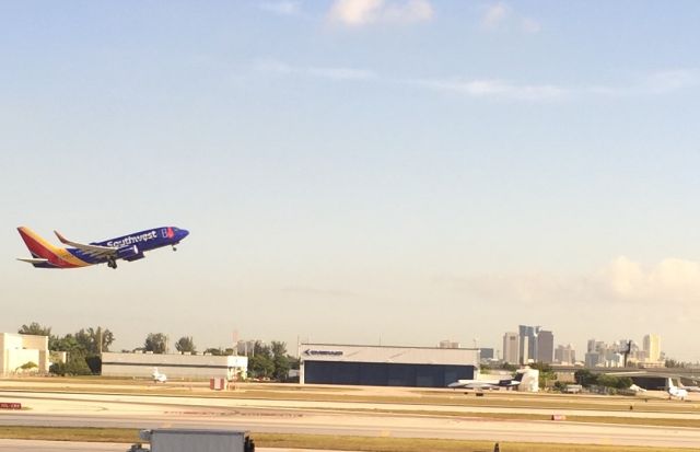 Boeing 737-700 — - Southwest 737 taking off above Embraer hangar with FLL skyline in background.