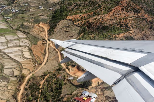 Airbus A319 (A5-RGF) - Steep climb followed by immediate banking to the left upon takeoff from Paro. Interesting artwork on the roof tops .... 4th April, 2015