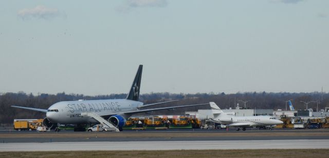 Boeing 777-200 (N218UA) - Catching some tarmac time is this member of the Star Alliance group, a 2001 United Airlines Boeing 777-222ER in the Winter of 2023.  Taxiing to parking is N990WR, a 1994 Dassault-Breguet Falcon 900B.