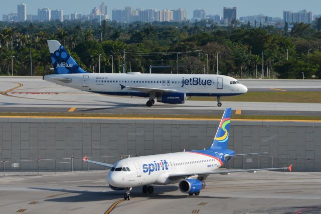 Airbus A320 (N665JB) - Taxiing in on sloped extension of RWY 28L, while Spirit A320-200 (N613NK) pulls into Terminal 4 below.