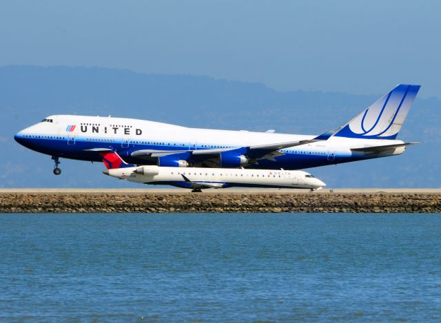 Boeing 747-200 (N107UA) - United Heavy touches down on 28R as Delta Connection flight 4597 taxis on foxtrot for 28L departure.