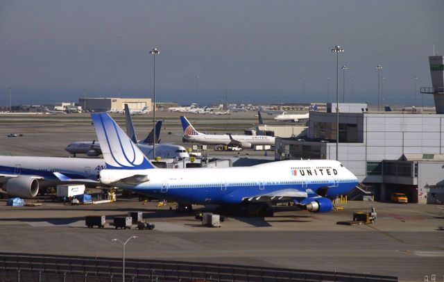 Boeing 747-400 (N105UA) - KSFO mid 2000 photo from the SFO tramway using the mobile platform to get a better angle than from the parking garage, N105UA wore a few paint jobs for UAL and this one is one of the better schemes. I rode the Tramway for quite awhile at SFO and was able to get many different aircraft and airlines using the Tram. The 747 is at Intl Terminal G.