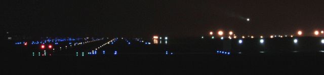 — — - Looking down runway 28 with the tower beacon shining through the fog and rain in the distance.