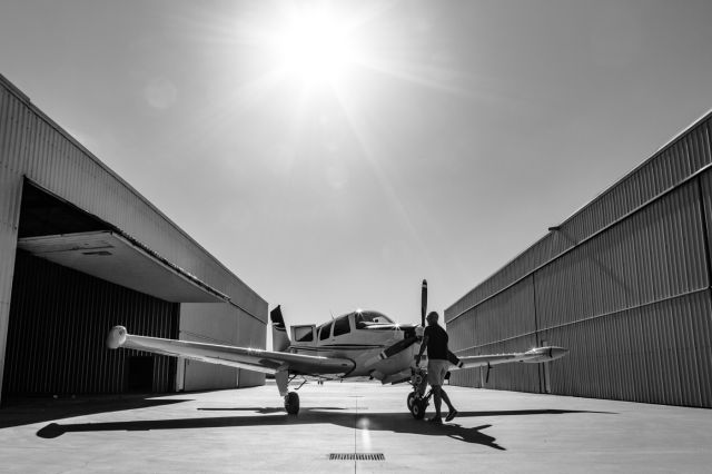 — — - A Bonanaza being pushed back into its hangar.