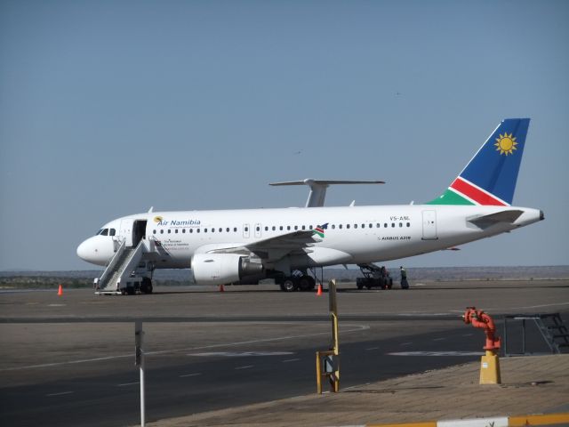 V5-ANL — - Eine der 4 neuen A319-100 der Air Namibia, ebenfalls am Nachmittag des 09.10.2011 auf dem Vorfeld WDH fotografiert. Im Hintergrund ist das riesige Seitenleitwerk der IL-76M UR-17618 der Air Almaty zu sehen, die am 07.10.2011 hier reinkam. 