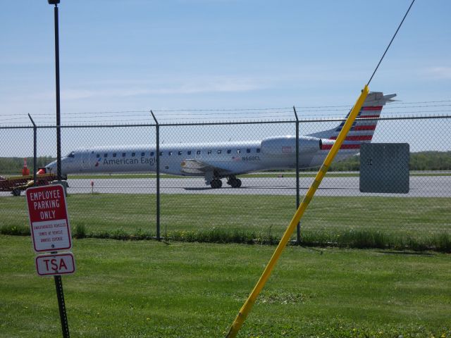 Embraer ERJ-145 (N660CL) - Shown here catching some tarmac time is a American Eagle ERJ-145 in the Spring of 2018. I have photographed this plane by coincidence at Philadelphia in the Autumn of 2017 and CYOW two days ago and one day ago the day after I decide to see what the airport in Watertown NY looks like it is the only plane at the very small terminal. br /Sorry, for my 1500 posting I could not block the shot anymore but how would the world survive without chain-link fence, signage, and utility pole supports? Nice lawn though!