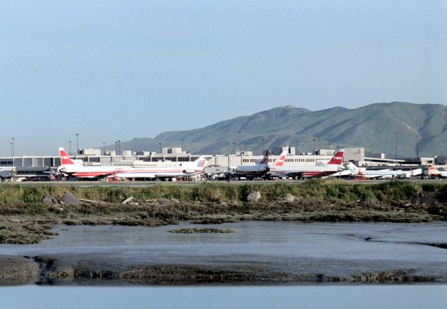 Lockheed L-1011 TriStar — - KSFO- TWA dock at SFO in 1988 - this must have been a Saturday or Sunday AM in spring, I'd get up early and head to SFO Air-park on Millbrae Ave and film all day and get some video too. This shows the older SFO terminal view before the fences were put up near the 1R departure runway. Note the Republic 727 and multiple TWA L1011's. Also of note, the painted So San Francisco sign in the foothills behind, needs paint...!!