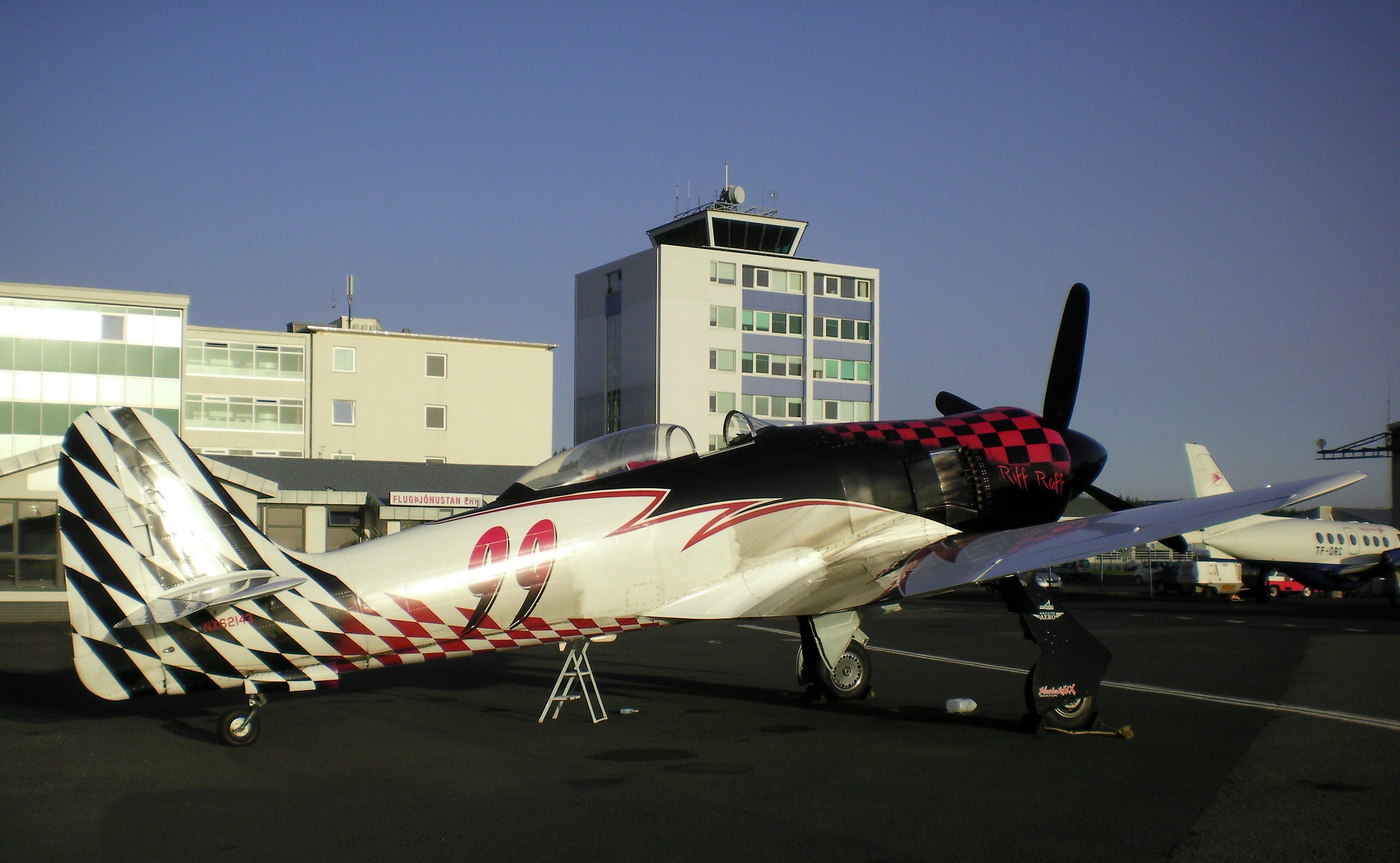 North American Fury (N62143) - RIFF-RAFF #99 (NX62143) was flown at the Reno Air Races by "Hoot Gibson" and is shown here at Reykjavik, Iceland. The Hawker Sea Fury made a fuel stop in Iceland and was enroute from KRFD to new owner in Czech Republic. ...In background is the Icelandair Natura Hotel and control tower at BIRK airport.