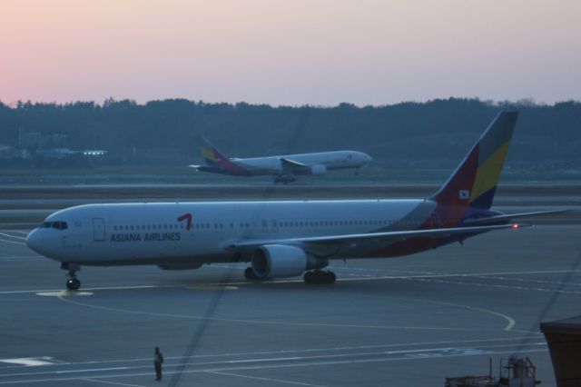 Airbus A330-300 — - An Asiana A330 touching down on Rnwy 34 at Incheon International Airport as another taxis to a gate.  Photographed just after sunset 01/16/2012.