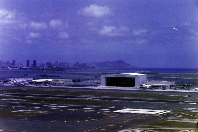 — — - PHNL- ATC Tower view of the south side of the airport. Note the jet departing from the Reef runway with views of Diamond Head and towards Waikiki Beach and downtown Honolulu. We were very lucky to get a tower tour and filming opportunity while here on vacation. July 1998.