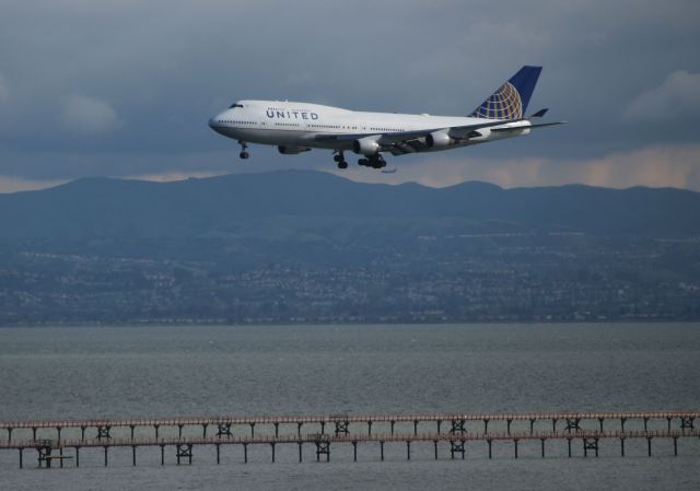 Boeing 747-400 (N177UA) - UA on short final from Beijing as showers loom in the background over Oakland