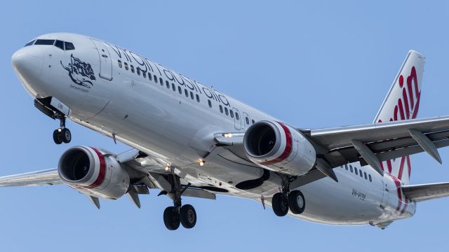 — — - A cloud rolls across the sun, helping accentuate the reflections in the fuselage and wings of this Virgin Oz, B738.