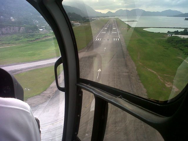 — — - Arriving back to the main island of Mahe the international airport's runway is before us as the helicopter makes its approach.