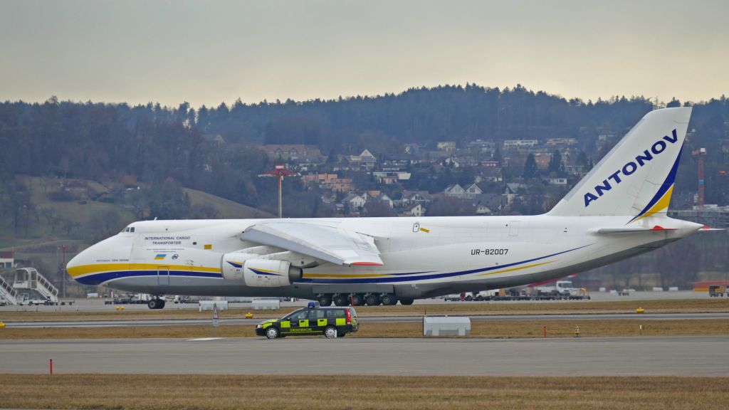 Antonov An-12 (UR-82007) - Taxiing for RWY 16 under the surveillance of security guards.