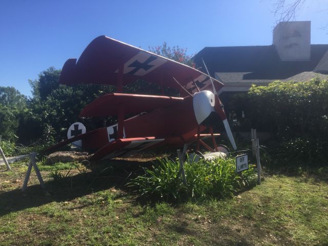 — — - A replica of the Red Barons Fokker triplane sits outside 94th Aero Squadron alongside Montgomery Field (MYF) in San Diego.