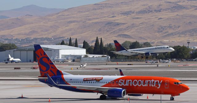 Boeing 737-800 (N833SY) - SCX's N833SY, wearing the "40 Years ..." special decal, sits on November ramp. In the background, a Delta Connection Embraer is about to touch down on RNO's only open runway (16R - 34L) while four GA aircraft (three of those are Great Basin Aviation's Cessnas) wait for it to land.
