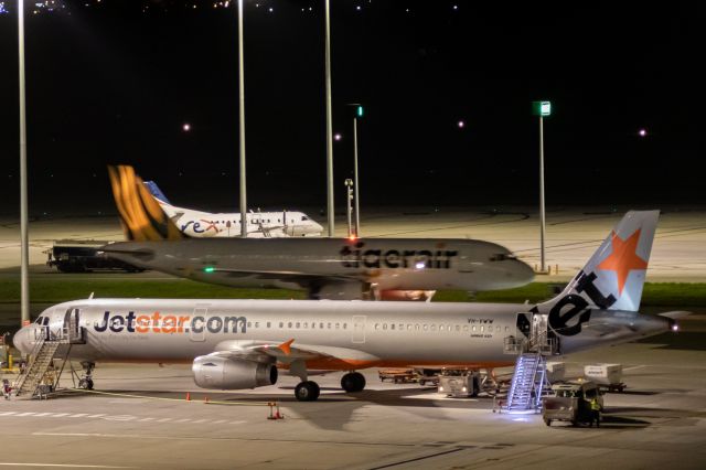 Airbus A321 (VH-VWW) - Jetstar A321 preparing for departure while Tiger A320 taxis behind, with REX S340 parked up for the night