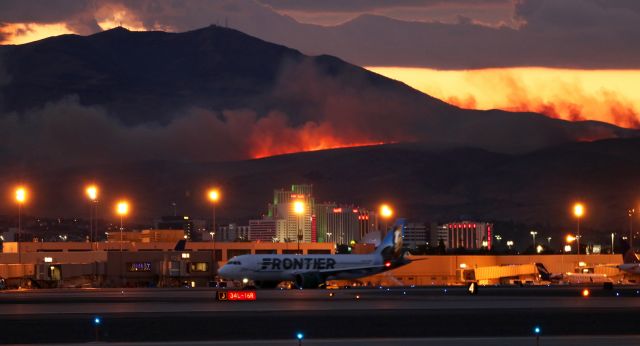 Airbus A320neo (N307FR) - It was a hot time in Reno last night. This photo, taken just 25 hours ago, catches FFTs "Champ the Bronco" (N307FR) hurriedly trying to taxi from the runway 16R hold line all the way down to the other end in an attempt to make it to runway 34L and get out of town. The Frontier flight had just left the terminal and was almost at the north end of taxiway Alpha, next to go from 16R, when sudden high swirling winds descended from the Sierra Nevada and a vicious electrical storm exploded over the airport and the city. An inbound SW, less than a mile out, encountered a brutal wind sheer and the pilots immediately reported that the flight was diverting to SMF. This Frontier Bus, a Navy C-40, and a FDX heavy all shut down their engines on Alpha to wait out the storm. As they sat, lightning ignited the fire visible here and a second fire just beginning to spread at the right edge of this photo. About 35-40 minutes later, after a UA inbound made a rough arrival on 34L, the FFT pilots requested permission to restart, swap ends of the runway, and get gone for Denver. This pic was taken as they hustled from the hold of 16R to 34L where they made a successful getaway.