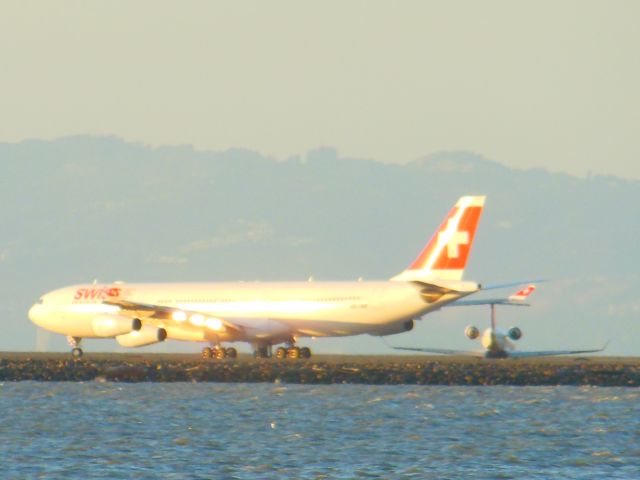 Airbus A340-300 (HB-JMA) - Evening sunlight brightening up this jet as a smaller Delta taxis, appearing to be wheel-less from this angle!