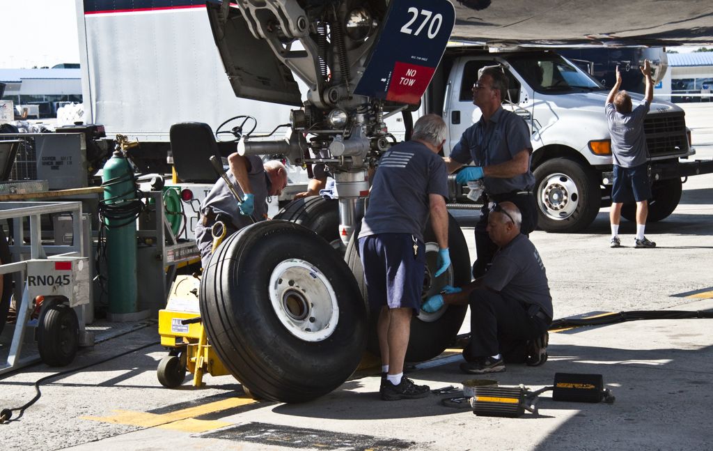 Airbus A330-300 (N270AY) - A "big bird" - Airbus A330-300 gets two new nose tires. Find five of your best AMT* friends, the tire cart & tug, four foot torque wrench, a fresh nitrogen bottle and that 85 ton jack. Oh, the airplane boards for Paris, France in about one hour...(rear-Catering is positioning their truck for meals delivery through right center service door) AMT: Aircraft Maintenance Technician; The new name for FAA certified Airframe and Powerplant Mechanics.