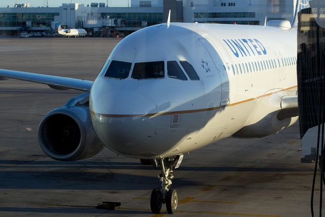 Airbus A320 (N484UA) - The jet bridge is being moved up and into position for this just-arrived A320 (N484UA) as the setting sun creates long shadows on the KDEN ramp.