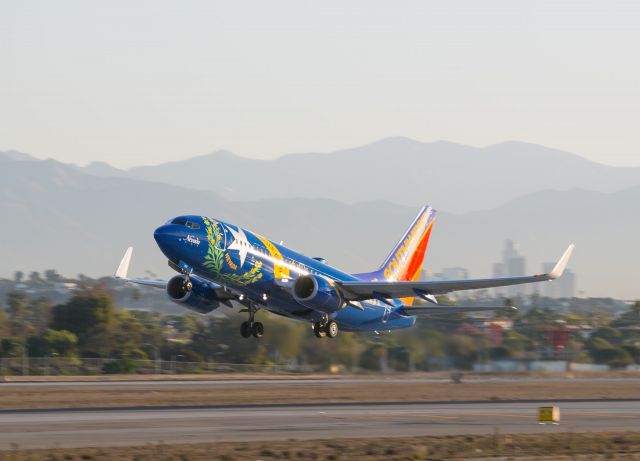 Boeing 737-700 (N727SW) - This custom painted Southwest Boeing 737 makes an early morning takeoff from their favorite LAX runway, 24 Left. It is painted in the design of the State Flag of Nevada. The capitol of that state is Reno, a detail overlooked when the Party Capitol of the World is Las Vega$. In this view looking northeast, downtown Los Angeles, California USA is visible in the background. The Hollywood area is about 12 miles away over the right wing tip. On a clear day the famous HOLLYWOOD sign can be seen from LAX.