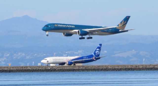 Boeing 737-900 (N265AK) - Vietnam Airlines landing on runway 28L while Alaska Airlines Honoring the Veterans Livery 737 taking off on 28R at SFO