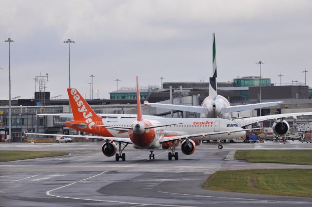Airbus A320 (G-EZUA) - Retro liveried A320 taxis out of T1 terminal at Manchester as another Easy rolls towards it & an Emirates A380 waits to push back for DXB