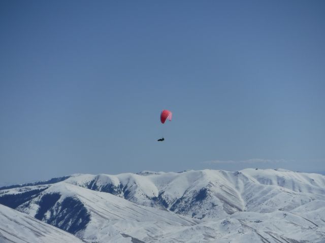 — — - Para Glider flying over Baldy Ski Hill in Sun Valley, Idaho with the Pioneer Mountains in the back Ground. 