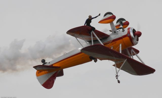 — — - Wing walker sitting on the underside of the lower wing during an inverted pass at Sun 'n Fun 2013.