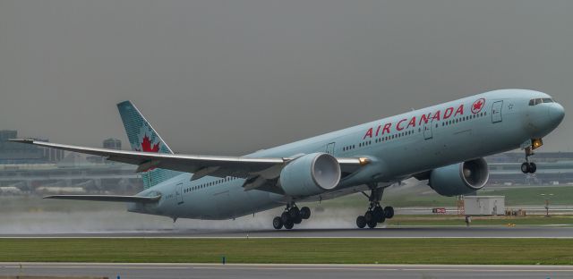 BOEING 777-300 (C-FIVQ) - Grim day for plane photography at YYZ… ACA87 lifts off a wet runway 23 on the start of her 14 hour journey to Shanghai with some fog brewing in the number two engine...